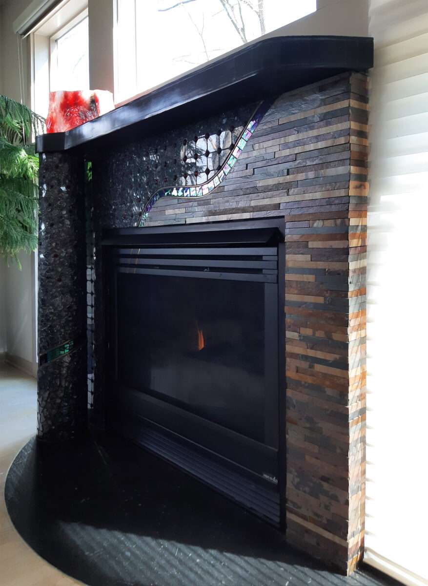 view of fireplace surround from right; horizontal strips of brownish slate; black mantel and apron, freestanding column on left