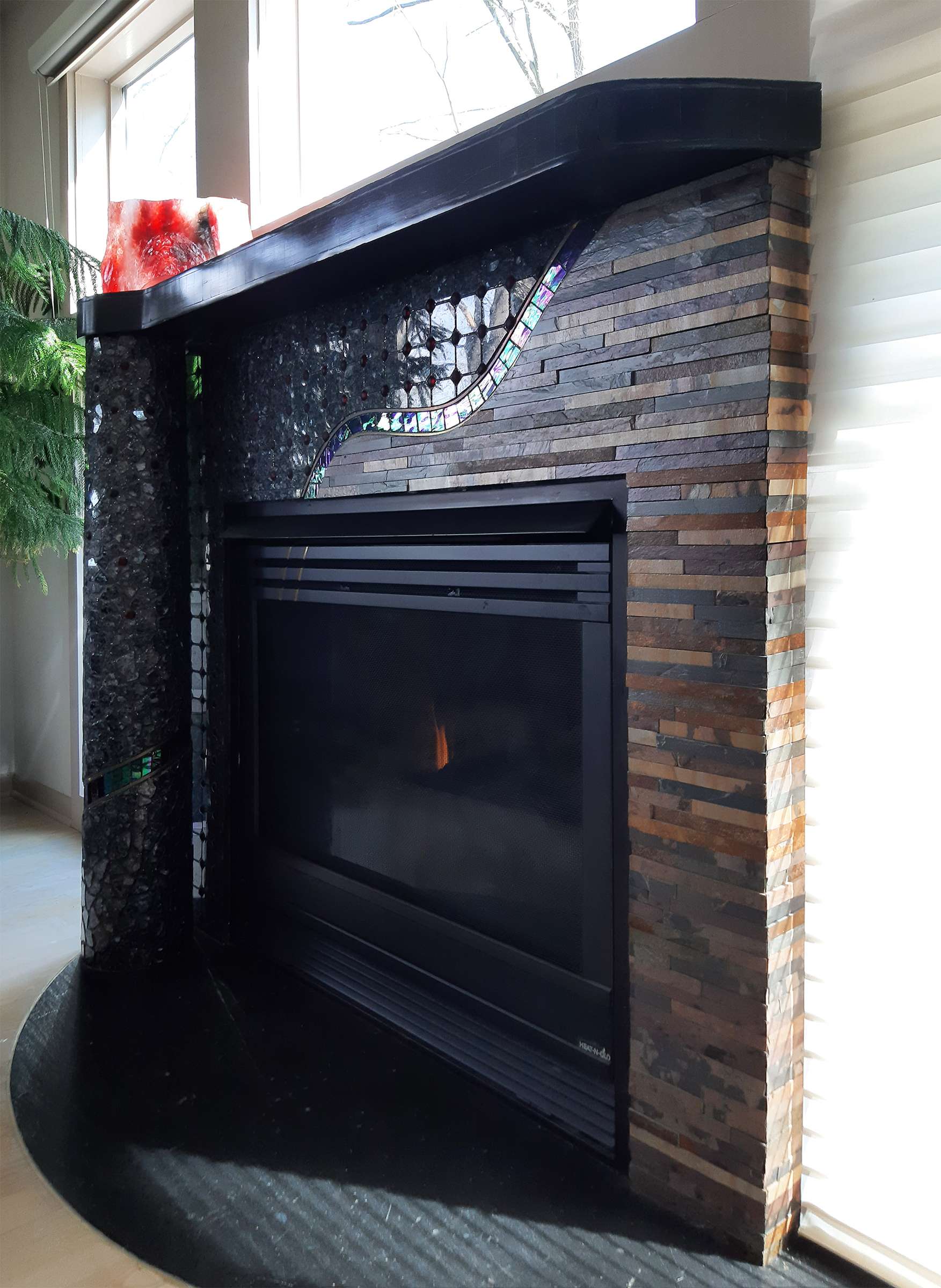 view of fireplace surround from right; horizontal strips of brownish slate; black mantel and apron, freestanding column on left